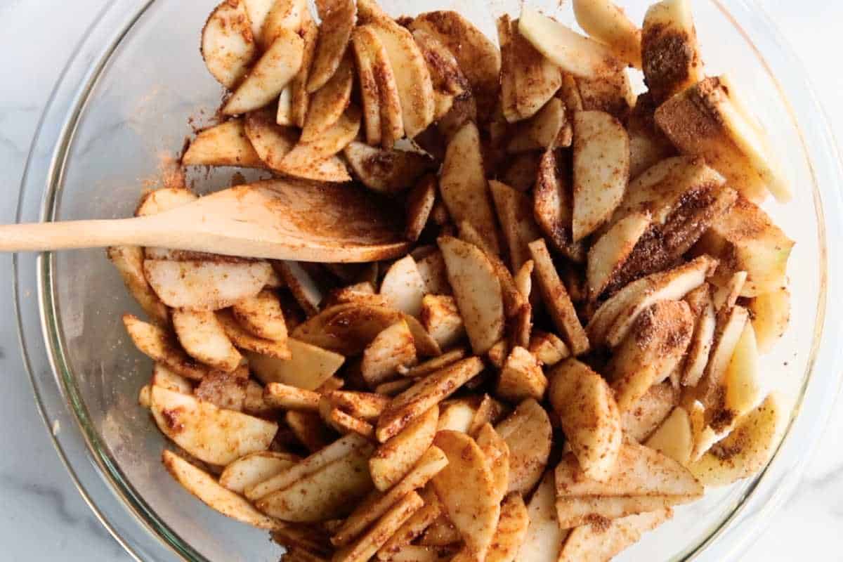 sliced apples in a large bowl with a wooden spoon.