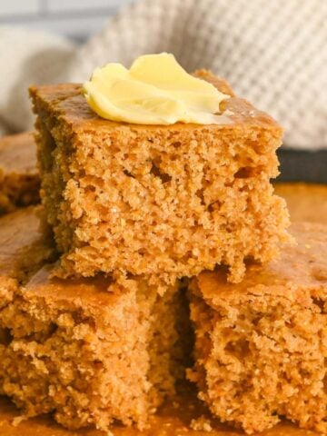 close up of three slices of cornbread in a stack with butter on the top.