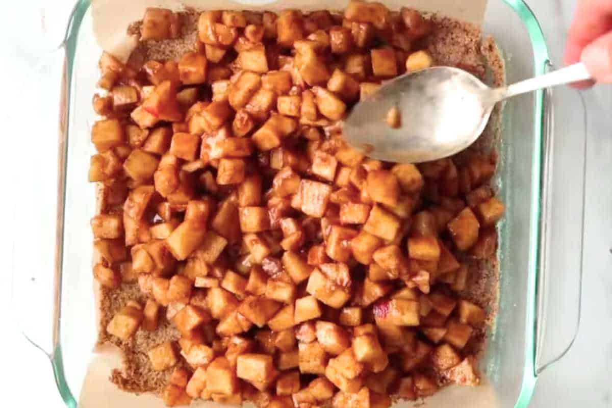 filling ingredients in a square glass dish with a spoon.