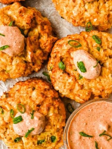 healthy air fryer crab cakes on white parchment paper topped with remoulade sauce and green onions.