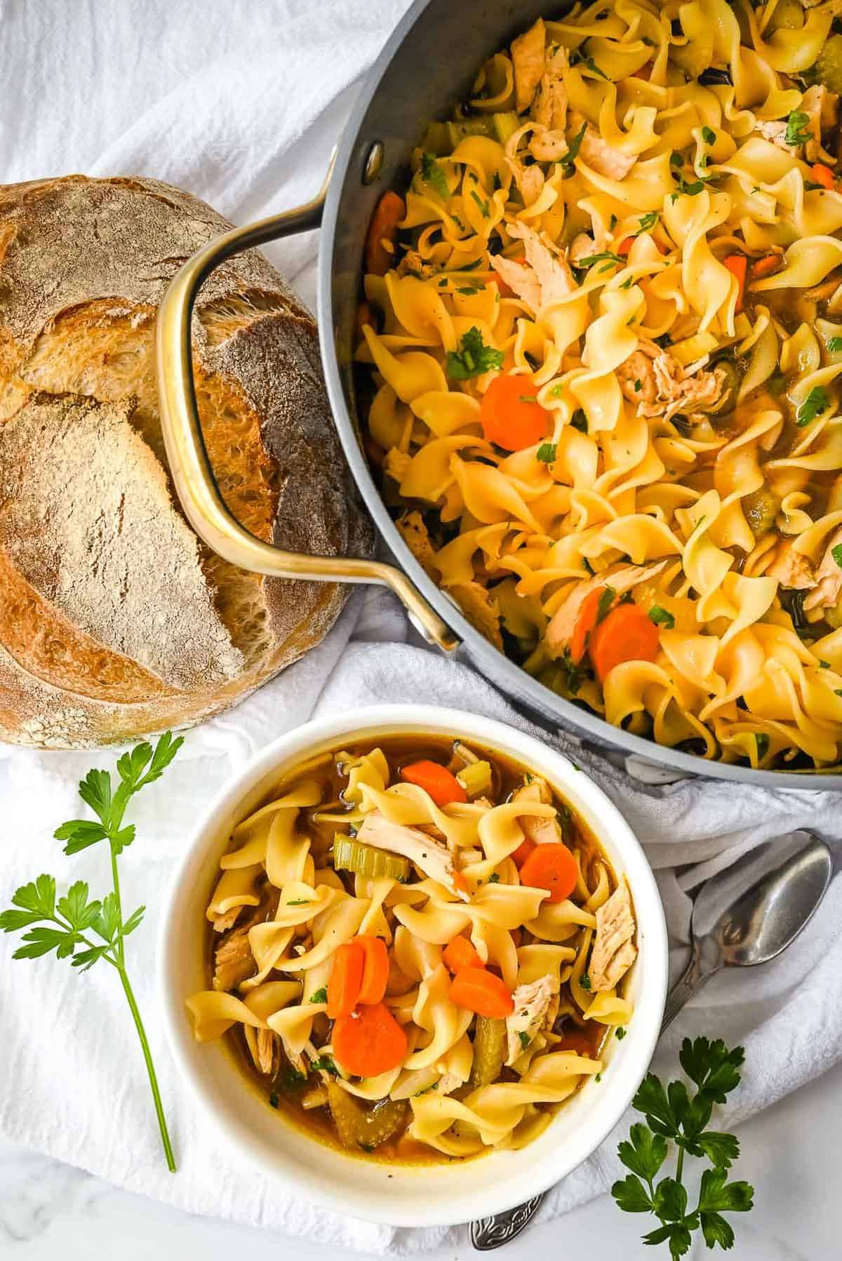 photo of bone broth chicken noodle soup in a bowl and a pot next to it with bread.