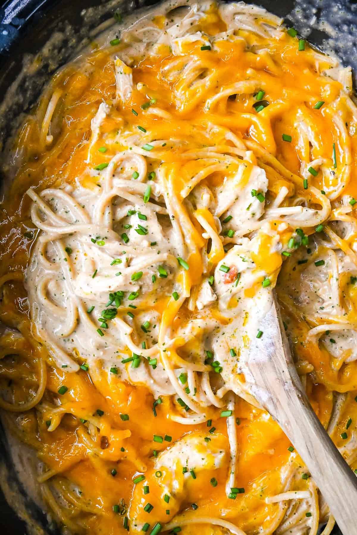 close up shot of crock pot chicken spaghetti with a wooden spoon.