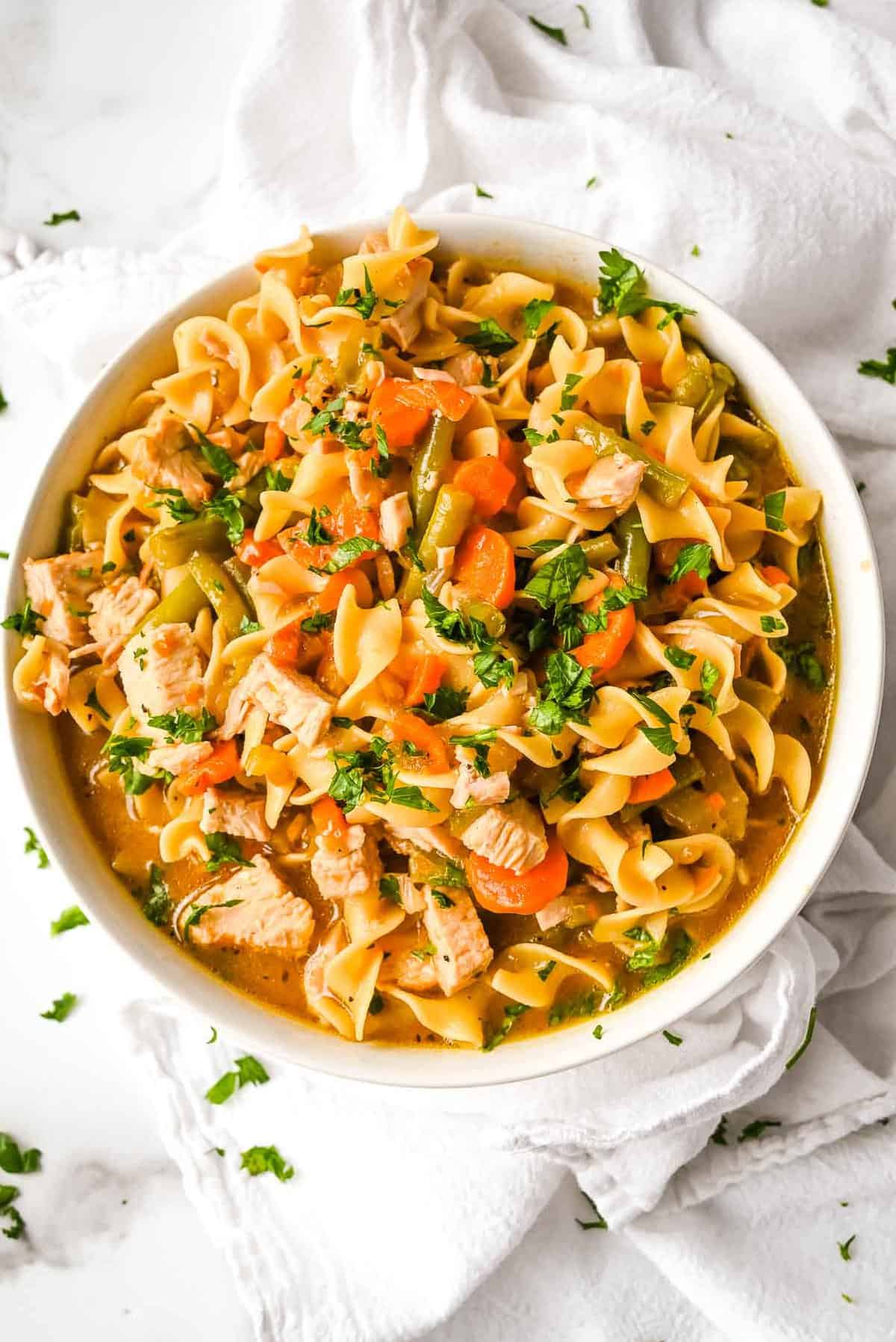 top down shot of instant pot turkey noodle soup topped with parsley on a white background.
