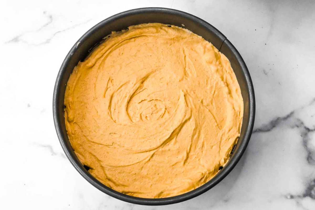 pumpkin cheesecake in a springform pan on a white marble background.