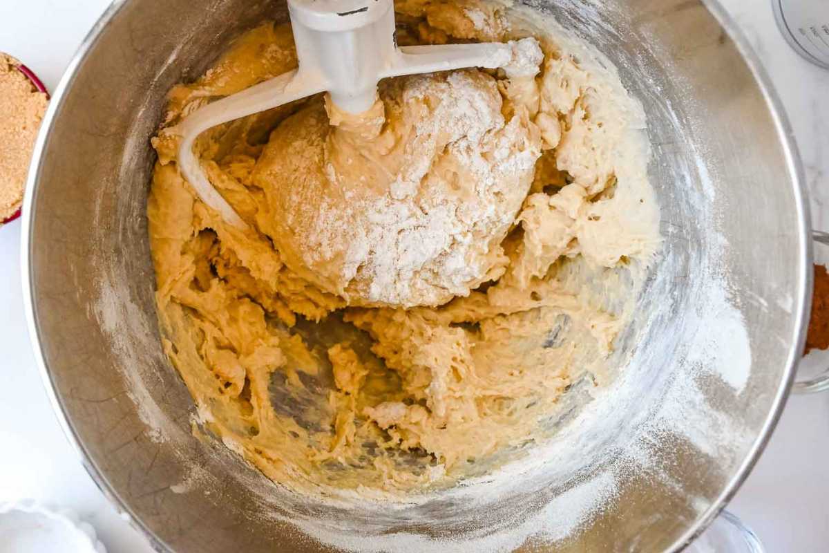 cinnamon roll dough in a silver bowl with a white paddle in it.