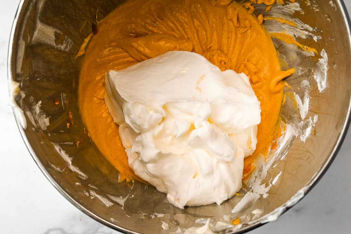 whipped cream on top of pumpkin cheesecake mixture in a silver bowl.