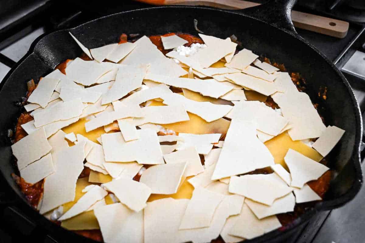 uncooked lasagna noodles broken on top of meat mixture in a cast iron skillet.