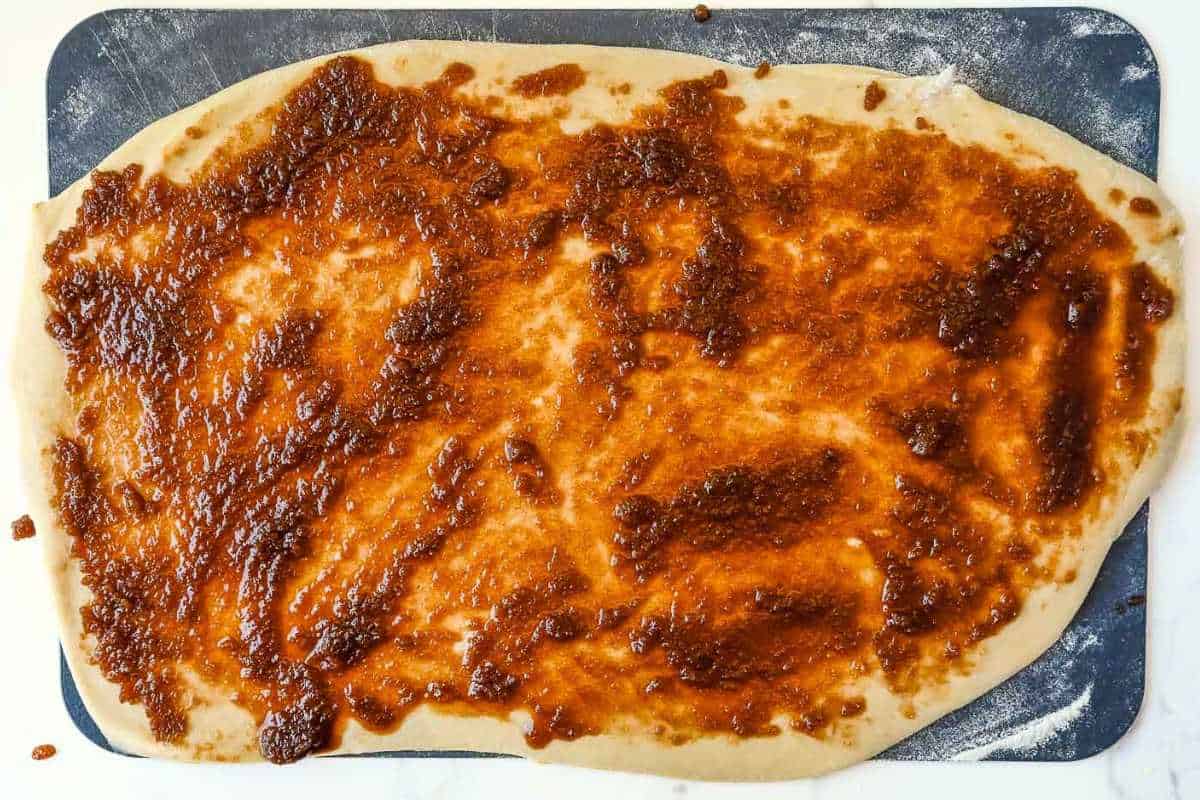 rolled out cinnamon roll dough on a black cutting board.