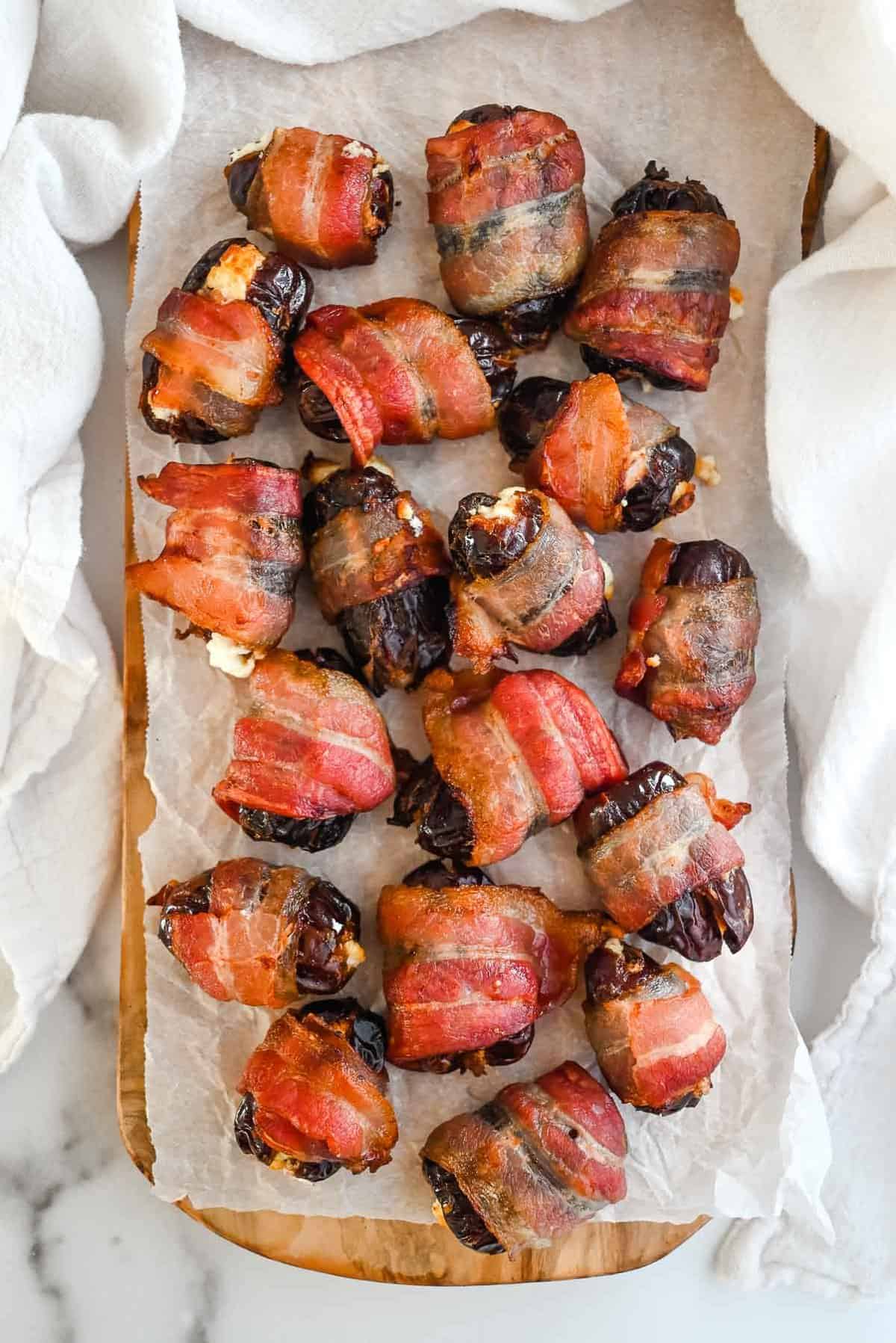 full shot of bacon wrapped goat cheese stuffed dates on white parchment paper.