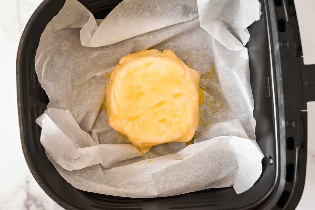 brie wheel on parchment paper in an air fryer basket.