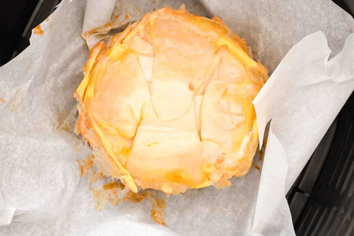 brie cheese flipped over in an air fryer basket.