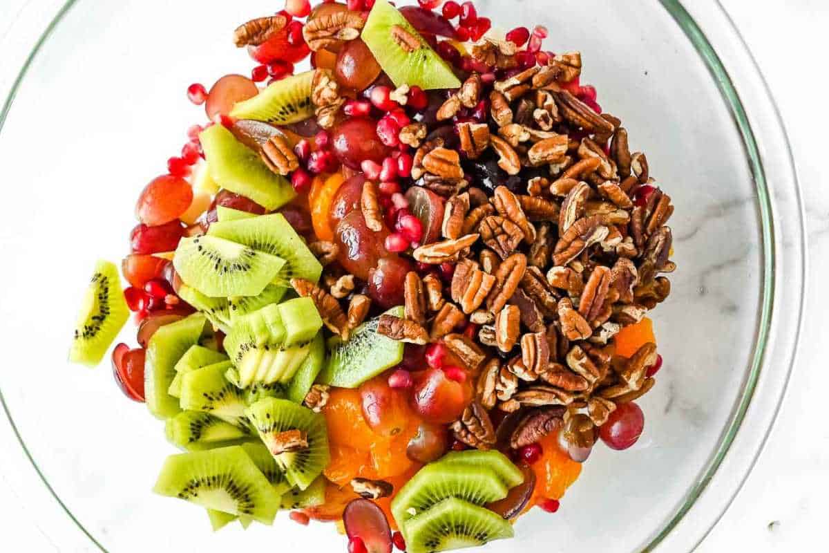 thanksgiving fruit salad ingredients in a glass bowl on a white background.