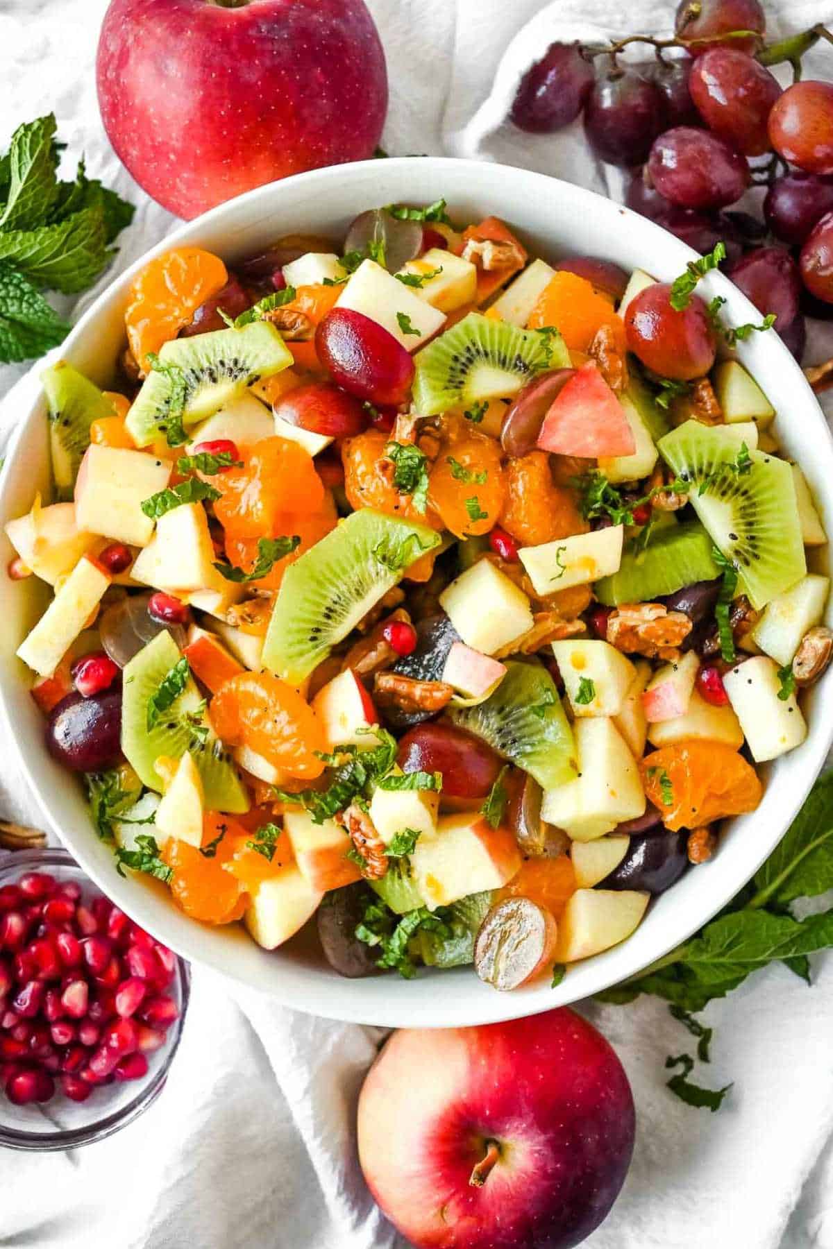 full shot of thanksgiving fruit salad in a white bowl with ingredients surrounding it.