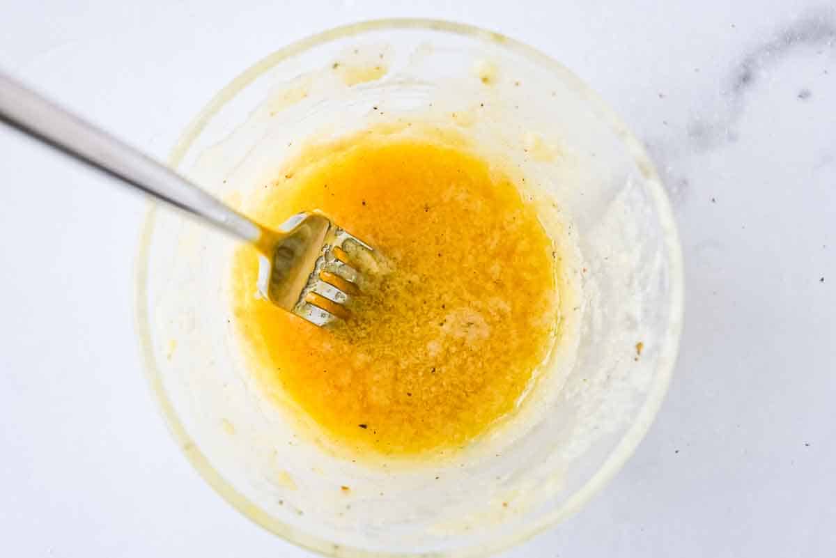 glass bowl of garlic butter sauce with a fork on a white marble background.