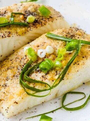 close up shot of air fryer halibut on a white plate topped with green onions and seasoning.