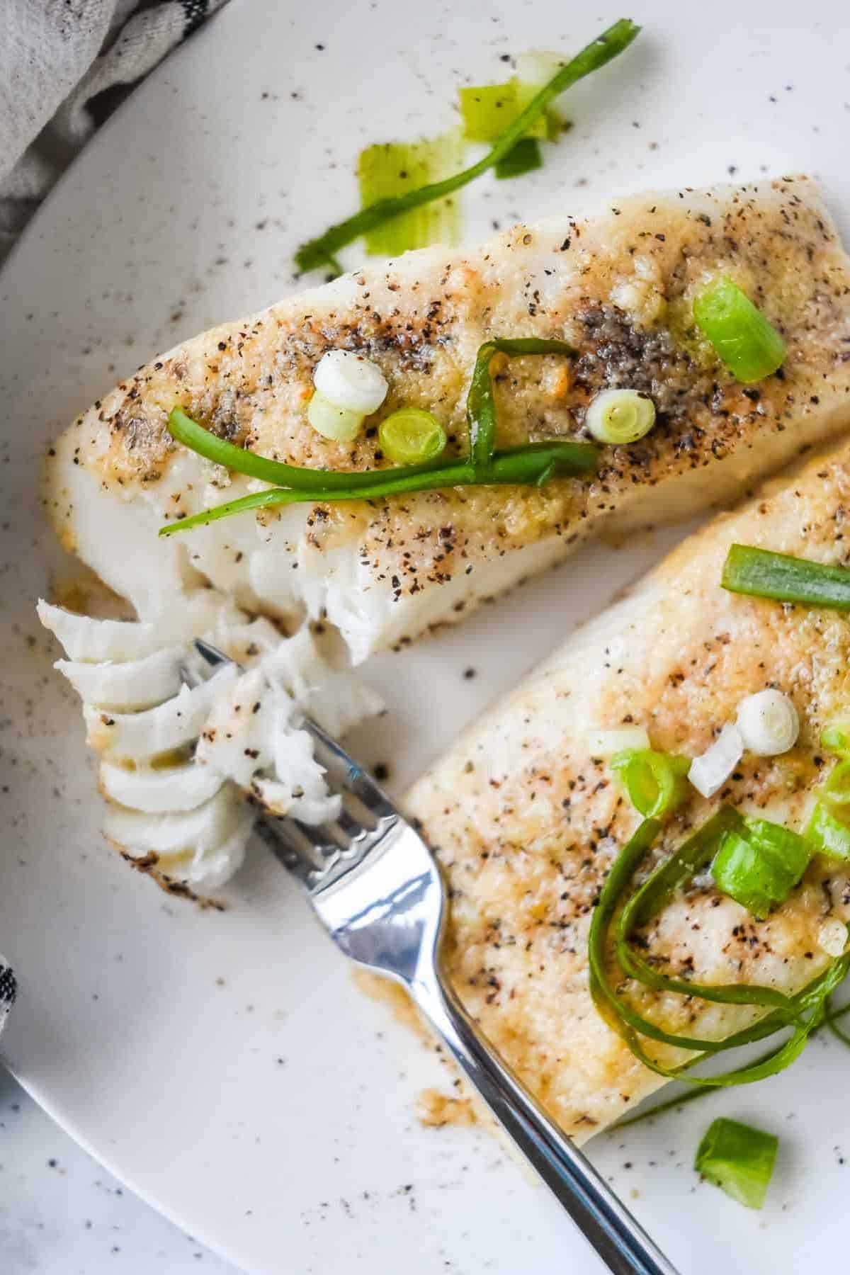 two fillets of air fryer halibut on a white plate with a fork of fish.