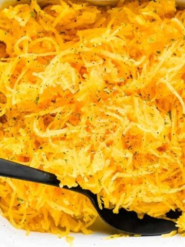 close up shot of air fryer spaghetti squash in a white casserole dish with a black spoon topped with parsley and pepper.
