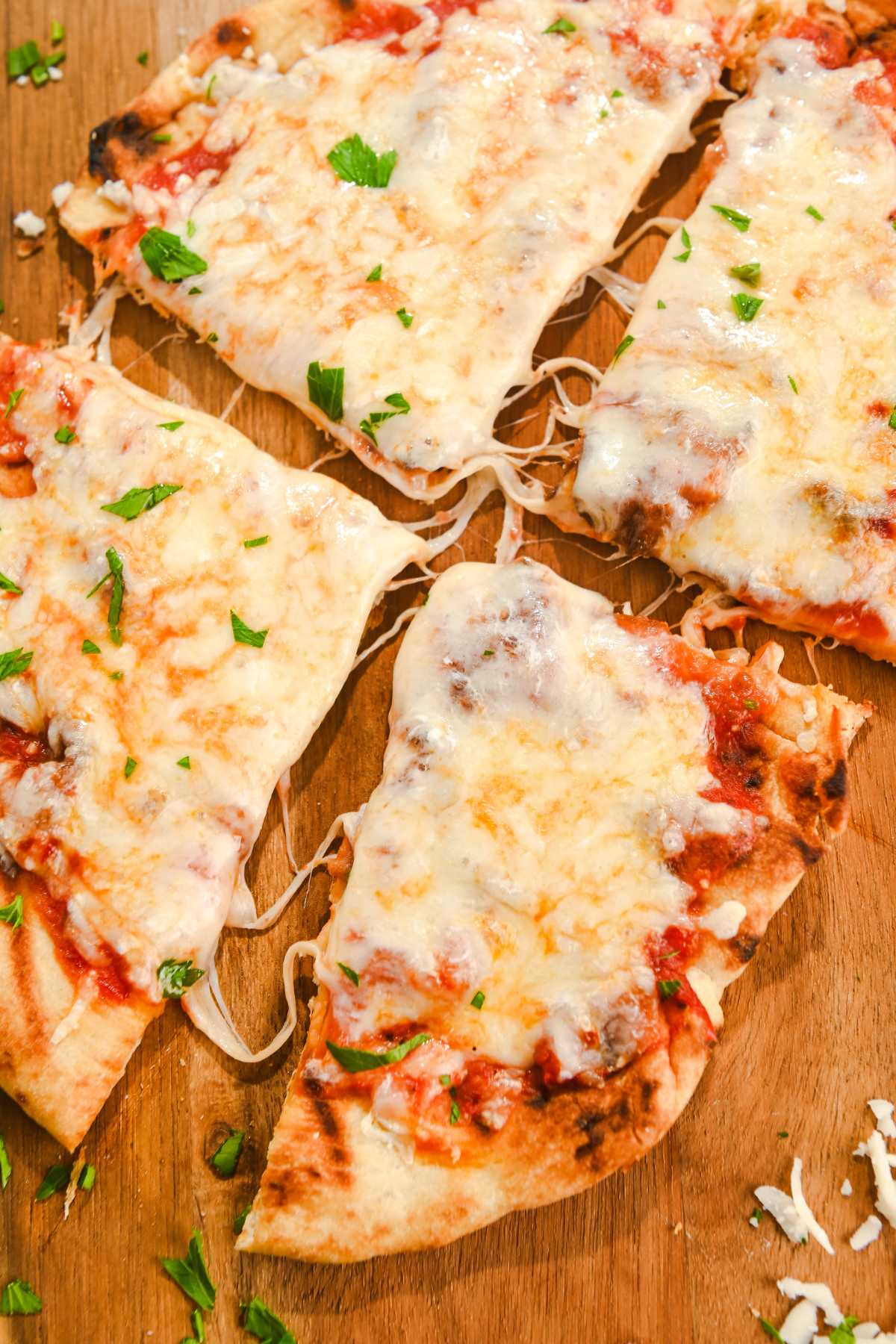 air fryer naan pizza cut into four pieces on a wood cutting board.