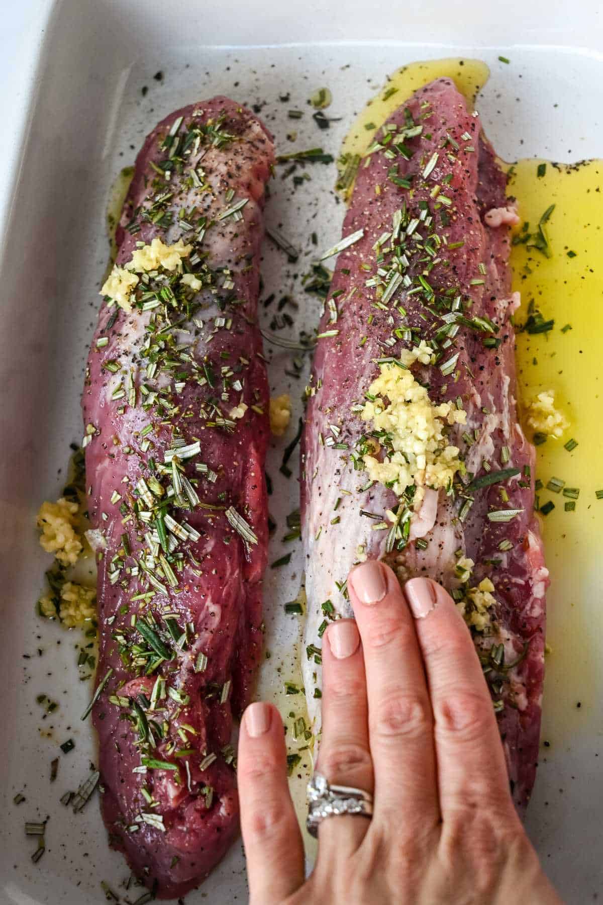 seasoning pork in a pan with garlic showing hand.
