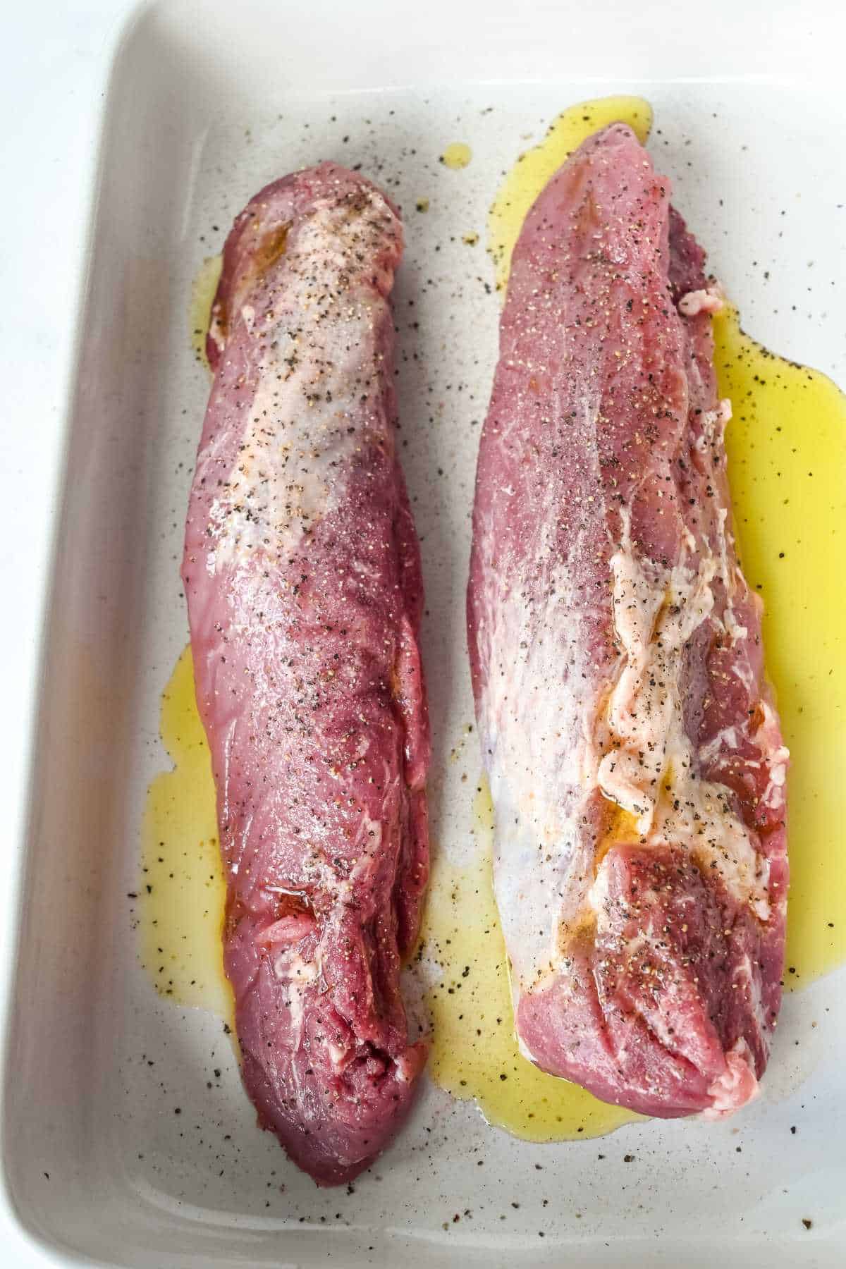 pork seasoned with salt and pepper in a white pan with olive oil.