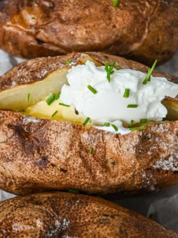 featured image showing close up of baked potato topped with sour cream, butter, and chives.