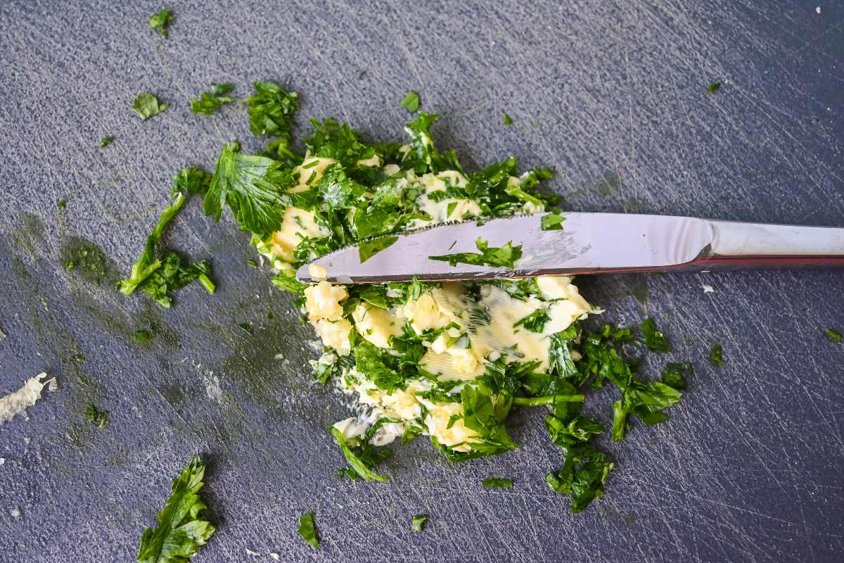 butter and herbs with a knife on a gray cutting board.