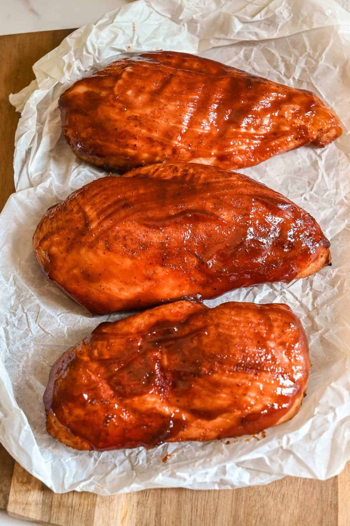 three bbq chicken breast on white parchment paper.