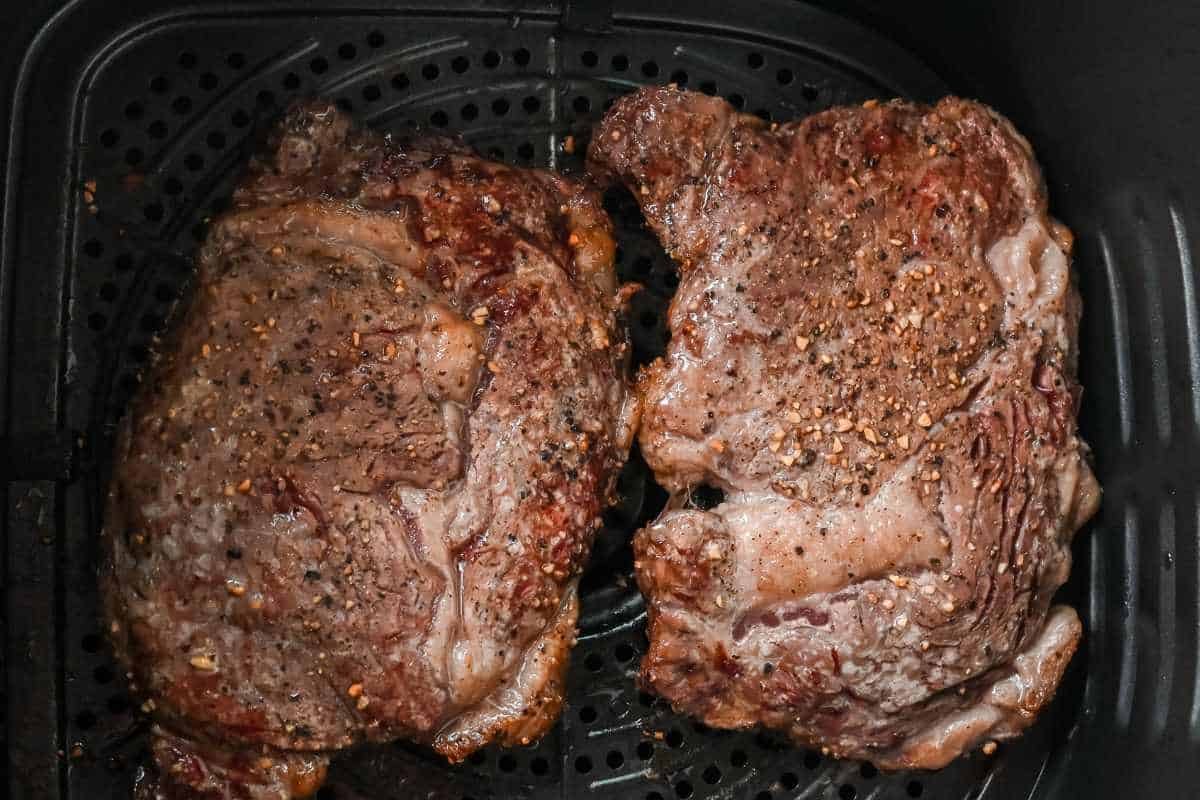 cooked ribeye in an air fryer basket.