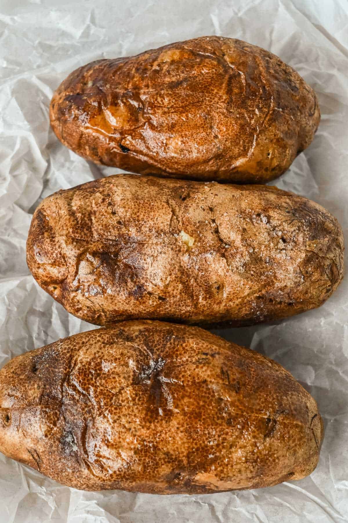 three baked potatoes on white parchment paper.
