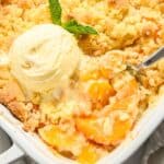 close up of peach cobbler in a white square dish with a scoop of ice cream on top and mint.