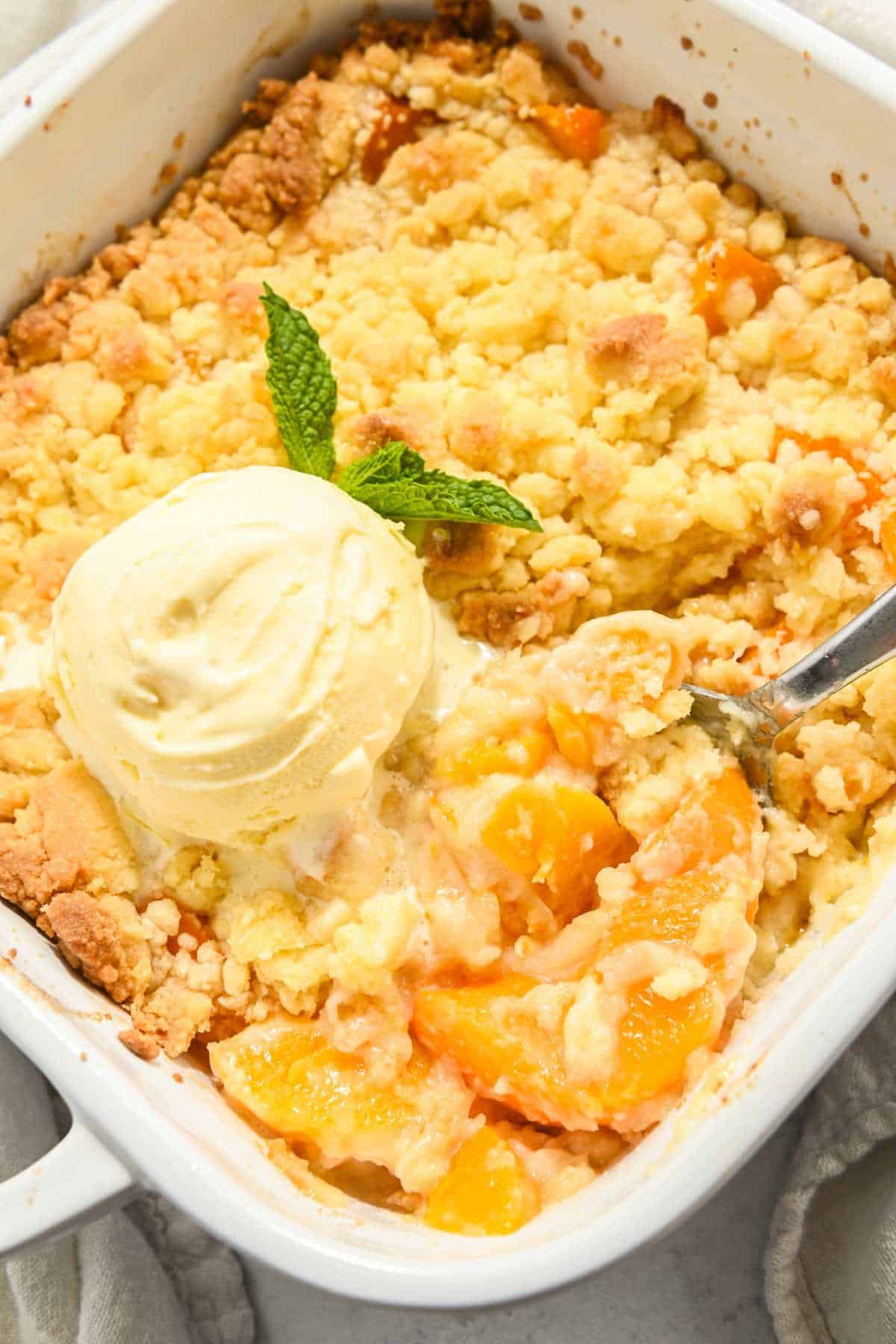 peach cobbler in a white square dish with a scoop of ice cream on top.