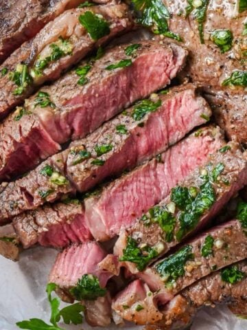 close up of sliced air fryer ribeye topped with butter and fresh herbs.
