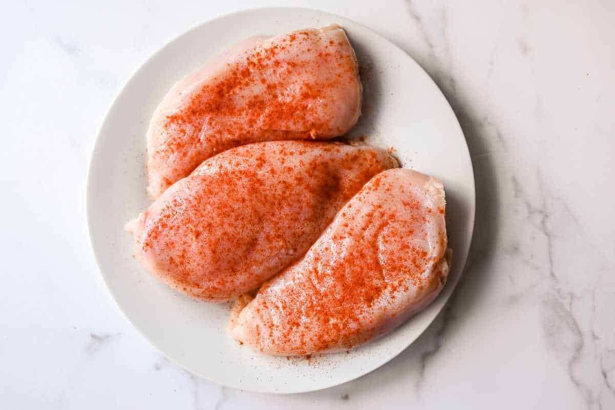 raw seasoned chicken breast on a white plate.