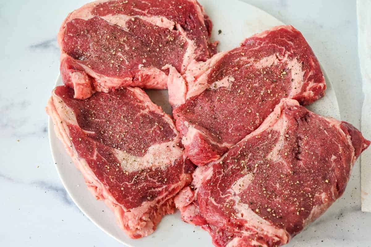 raw seasoned ribeye steak on a white plate.
