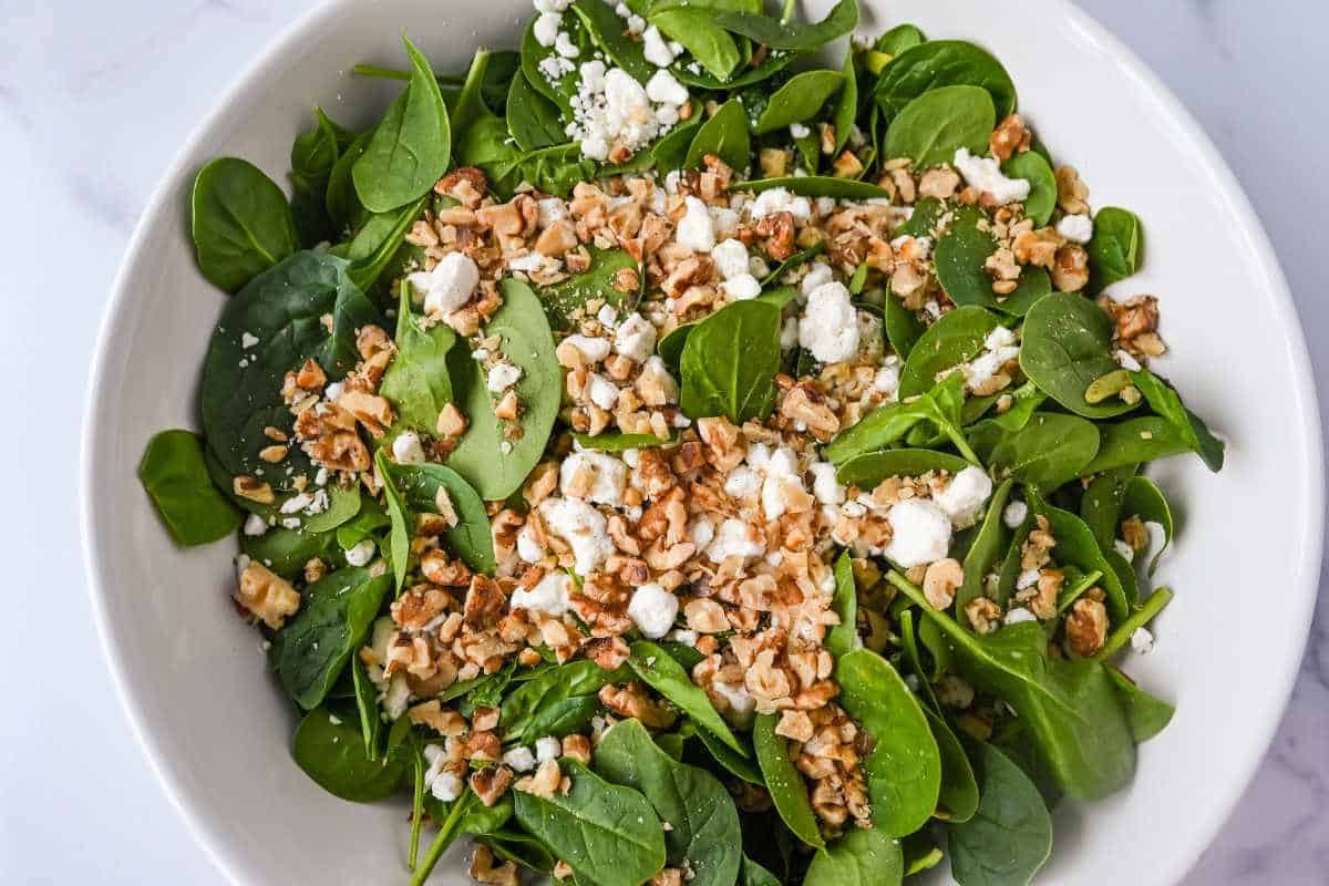 goat cheese and walnuts over spinach in a white bowl.