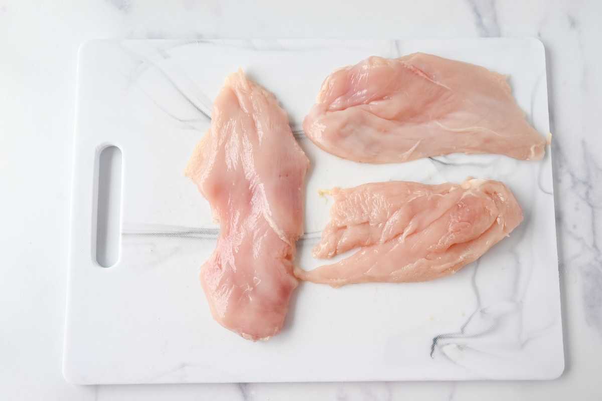raw chicken cutlets on a white cutting board.