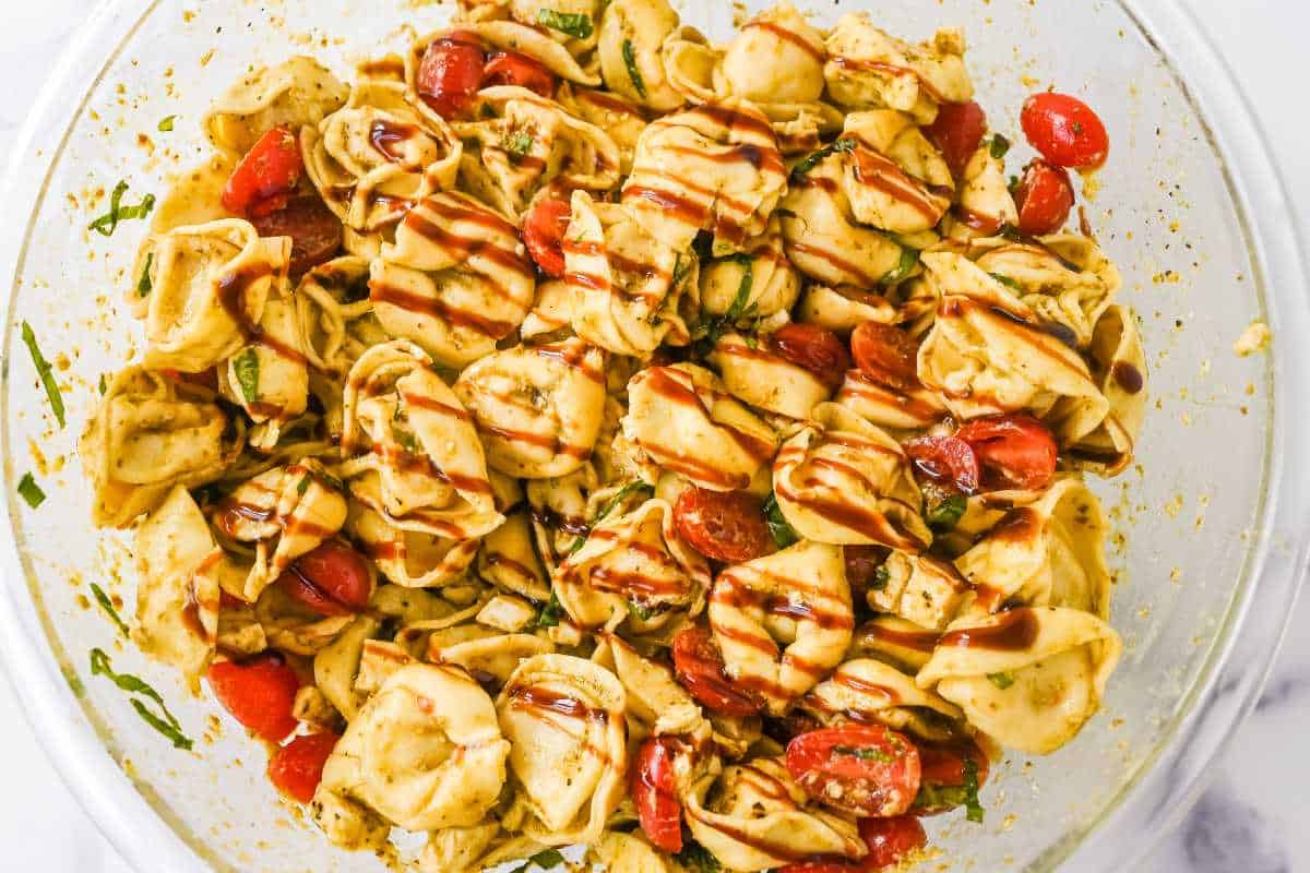 pesto tortellini salad topped with balsamic glaze in a glass bowl.
