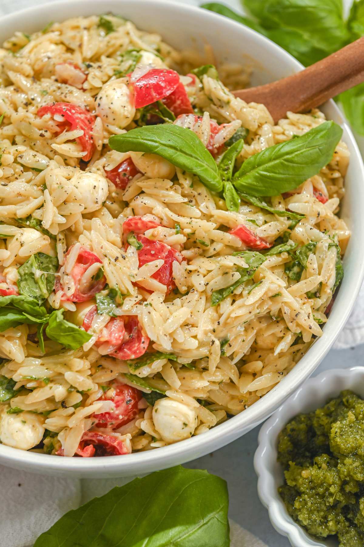 close up of basil pesto orzo salad with cherry tomatoes and basil leaves.