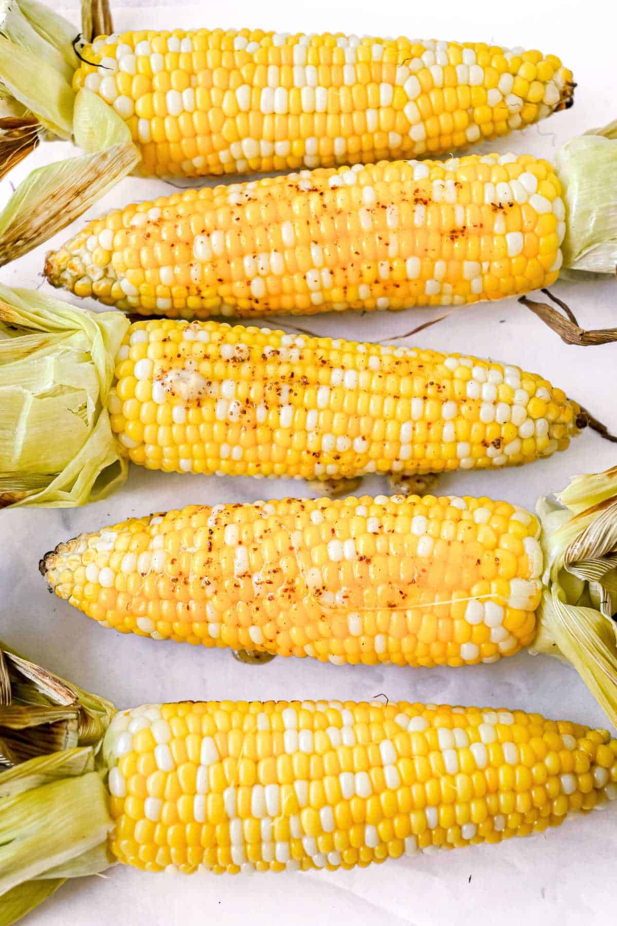 5 ears of corn with chili lime butter on top on a white background.