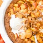 close up of nectarine cobbler in a white pie plate topped with vanilla ice cream with a spoon.