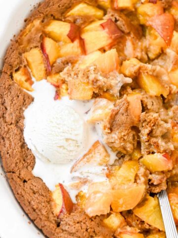 close up of nectarine cobbler in a white pie plate topped with vanilla ice cream with a spoon.