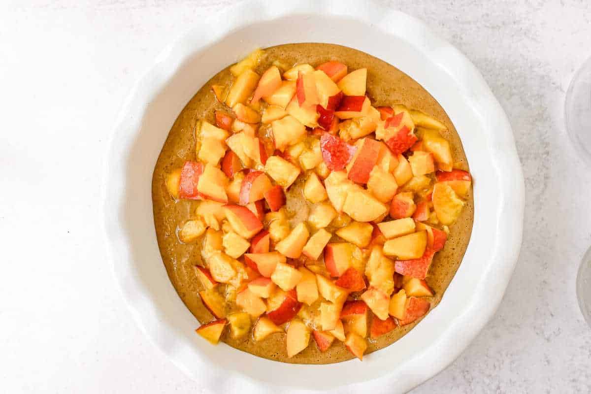 unbaked nectarine cobbler in a white pie plate on a light gray background.