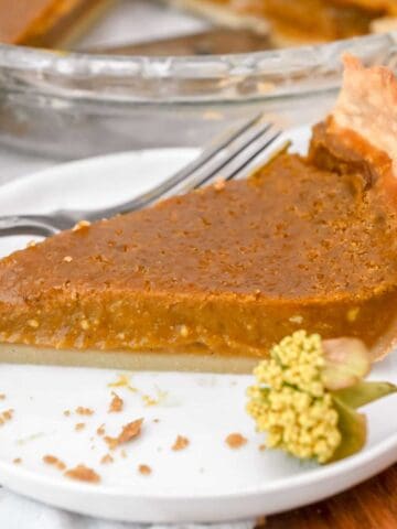 slice of eggless pumpkin pie on a white plate with a yellow flower next it.