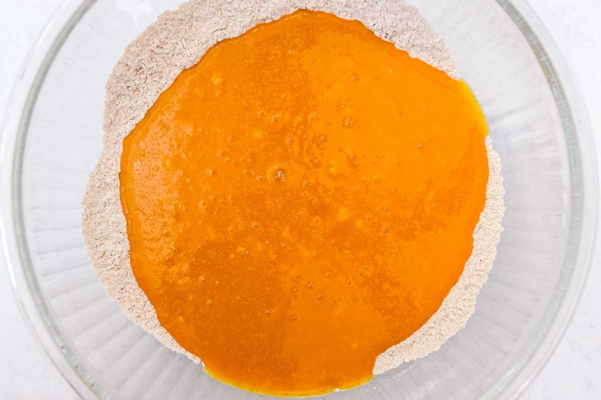 dry ingredients with wet ingredients on top in a glass bowl on a light gray background.