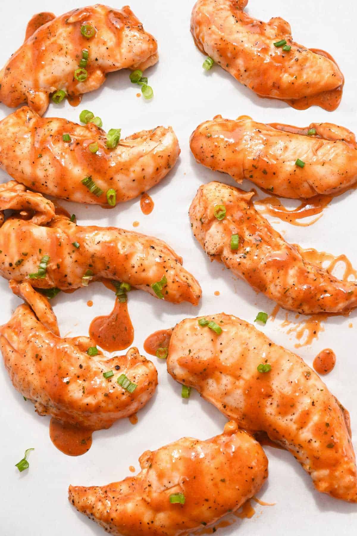 chicken tenders on a white background coated with frank's buffalo wing sauce.