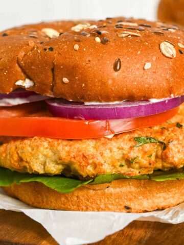 close up of air fryer chicken burgers on a bun with onion, lettuce, and tomato.