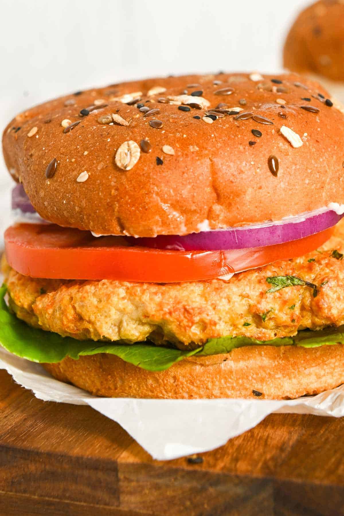 full view close up of air fryer chicken burgers on a bun with onion, lettuce, and tomato.