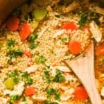 close up of chicken pastina soup with carrots and celery topped with parsley with a wooden spoon on top.