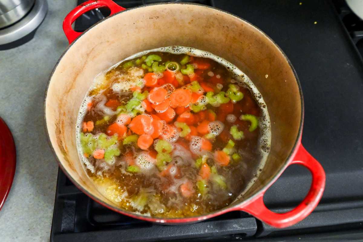 carrots and celery cooking in broth in a red pot.