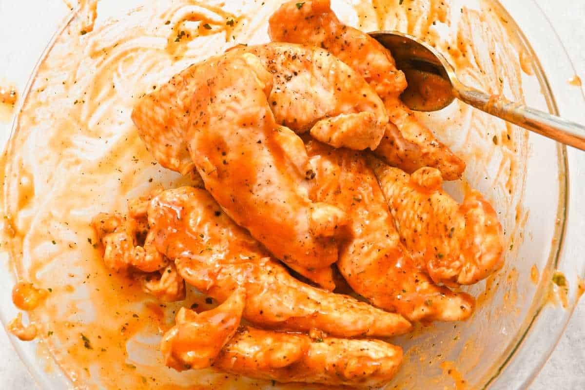no breading chicken tenders in a glass bowl with buffalo wing sauce.